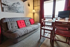 A cozy room with a grey sofa, red cushions, a wooden table, and a TV. - 12nd floor, balcony, tv, 21m², Chamrousse (Chamrousse)