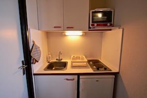 A compact kitchenette with a sink, a small stove, and a microwave above it.