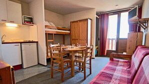 Una habitación compacta con literas, una kitchenette pequeña, una mesa de comedor con sillas y un sofá.