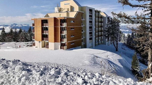 Ein modernes Hotel mit Holzfassade und mehreren Balkonen, umgeben von Schnee und Bäumen.