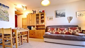 Ein gemütliches Wohnzimmer mit einem Holzesstisch, einer Couch mit gemusterten Kissen und einer Vitrine mit Glastüren.