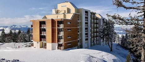 A multi-story hotel with a modern design, located in a snowy mountainous area.