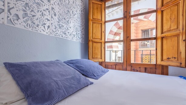Una cama con dos almohadas, una pared blanca y una ventana con contraventanas de madera.