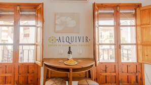 Una mesa de madera con una botella y copas, un cartel que dice "ALQUIVIR Gestión de Alojamientos Turísticos", y puertas de madera con ventanas.