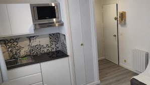 A compact kitchen with a microwave, a sink, and patterned backsplash. There is a door leading to another room and a radiator on the wall.