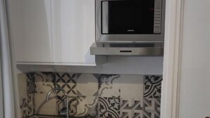 A compact kitchen with white cabinets, a microwave, and a patterned backsplash.