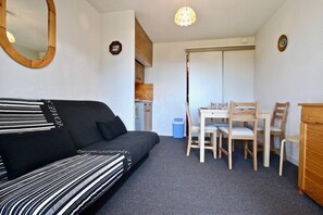 A compact living space with a sofa, dining table, chairs, and a small kitchenette.