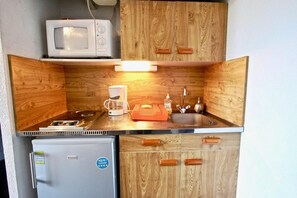 A compact kitchenette with a microwave, coffee maker, sink, and a small refrigerator.