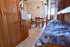 A bedroom with a bed, wooden wardrobe, and a desk with chairs.