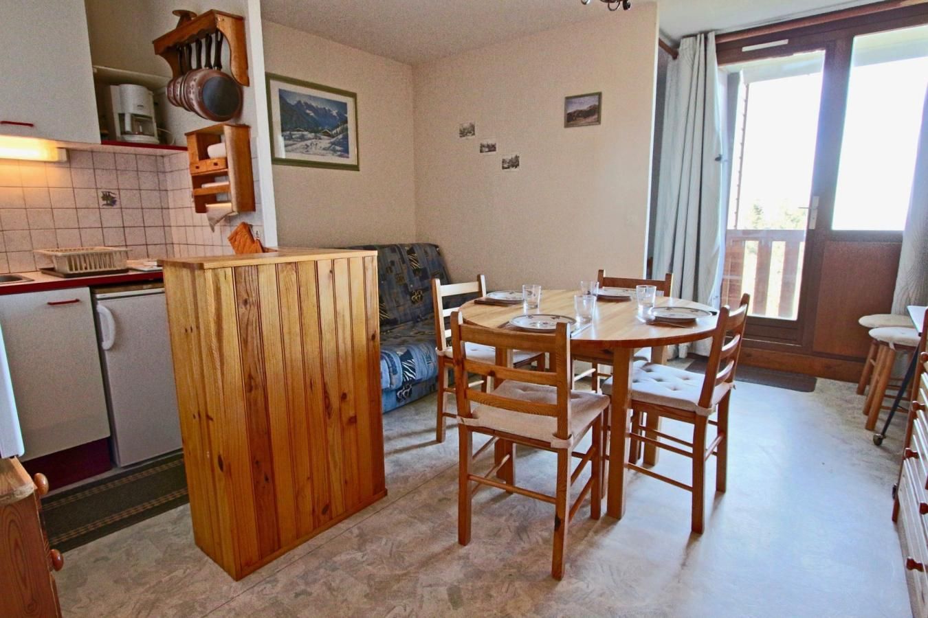 A compact kitchen with a dining area, a sofa, and a view through a glass door.