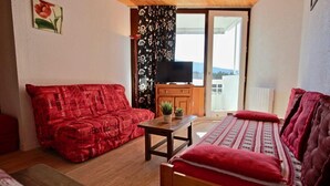 A cozy living room with a red sofa, a wooden table with a plant, and a bed with red bedding. - 300m from ski slopes, 6th floor, balcony, tv, 27m², Chamrousse (Chamrousse)