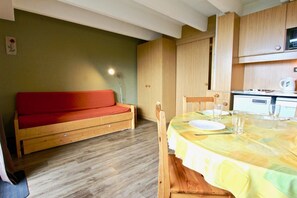 Une pièce chaleureuse avec un canapé en bois, une table à manger dressée avec des assiettes et des verres, et un coin cuisine en arrière-plan.