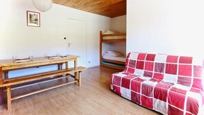 Une pièce avec une table en bois, des lits superposés et un canapé à carreaux rouges et blancs.
