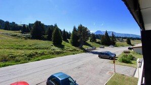 Un parking avec des voitures, un bâtiment doté d’un toit en pente et un paysage montagneux en arrière-plan.
