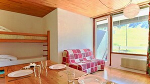 A cozy room with a wooden table set for dining, a bunk bed, and a window with a view of greenery.