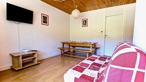 A room with a wooden ceiling, a wooden bench, a table with glasses, a television, and a door.