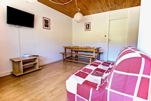 A room with a wooden ceiling, a wooden bench, a table with glasses, a television, and a door.