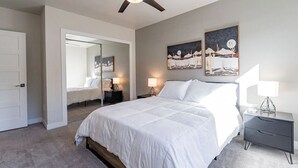 Een slaapkamer met een groot bed, twee nachtkastjes met lampen, een plafondventilator en kunstwerken aan de muren.