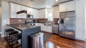 Een moderne keuken met witte kasten, een roestvrijstalen koelkast, een backsplash van baksteen en een centraal kookeiland met barkrukken.