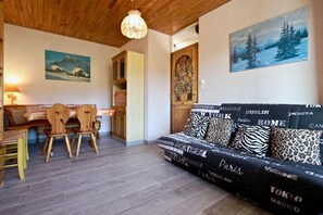 A cozy living room with a sofa adorned with city names, a dining area with wooden chairs, and a painting of a snowy landscape.