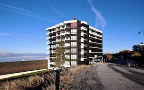 A multi-story building with balconies, a clear sky, and a view of the landscape.