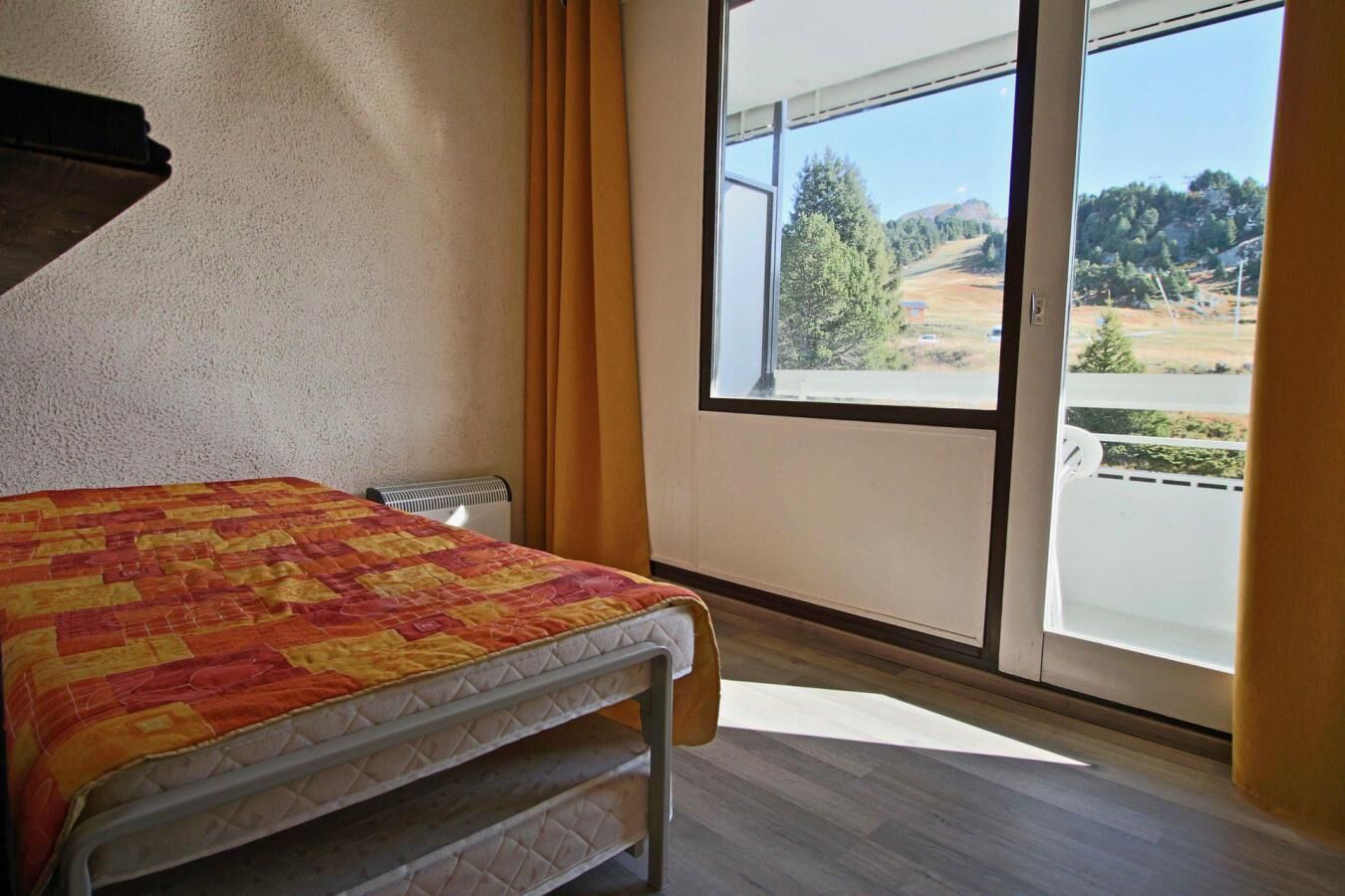 Ein Zimmer mit einem Bett, einem Heizkörper, einem Fenster mit Vorhängen und Blick auf eine Landschaft.