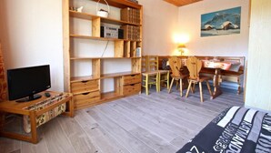 Une pièce chaleureuse avec un meuble TV en bois, une bibliothèque, un coin repas avec des chaises et un tableau accroché au mur.