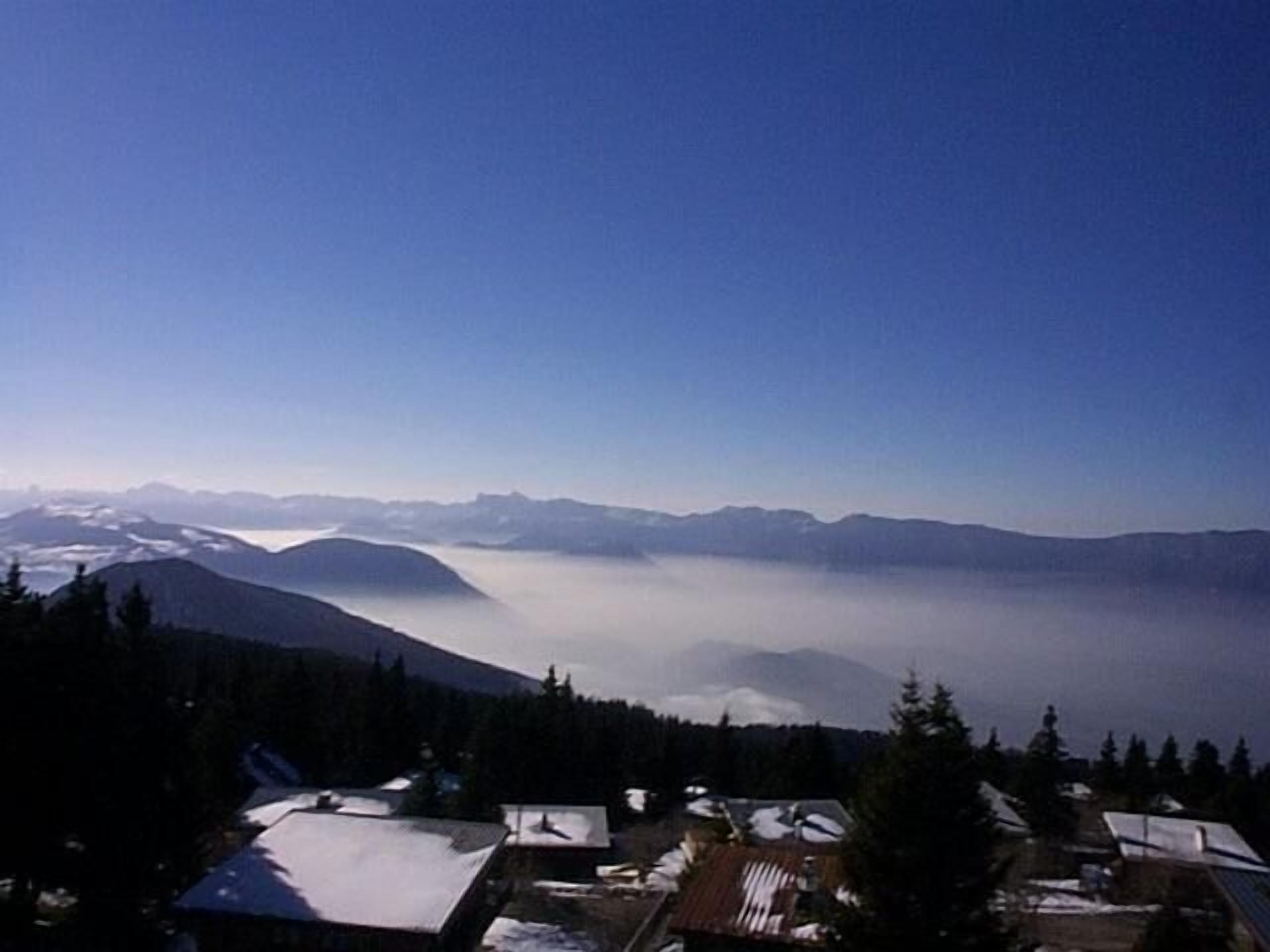 Un village de montagne aux toits et aux maisons couverts de neige, entouré de forêts et de montagnes.
