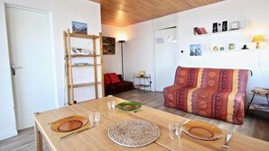 Un salon chaleureux avec une table en bois dressée pour le repas, un canapé agrémenté d’un plaid à motifs et une échelle appuyée contre le mur.