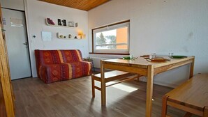 Une pièce chaleureuse avec une table à manger en bois, un canapé et une fenêtre donnant sur l’extérieur.