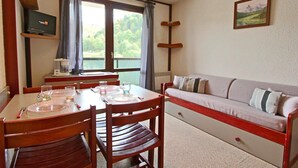 Un comedor con una mesa dispuesta para dos personas, un sofá y un televisor sobre una estantería.
