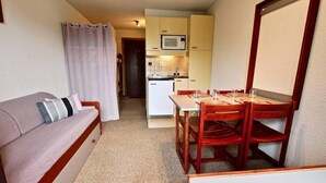 Un espacio habitable compacto con kitchenette, comedor y sofá con almohadones.