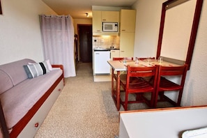 Een knus verblijf met een kitchenette, een eethoek en een bank met kussens.
