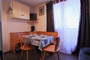 Un pequeño comedor con una mesa y sillas de madera, un televisor sobre la mesa y una ventana con cortinas.