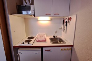 A compact kitchenette with a stove, sink, and a microwave above the counter.