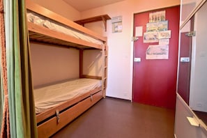 A bunk bed room with a red door and a bulletin board with pictures.