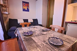 A dining area with a table set for two, a sofa, and a small kitchenette.