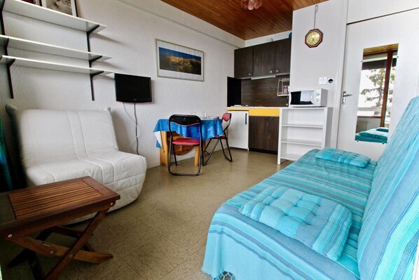 Een kamer met een bank, een kleine tafel, een kitchenette en een eethoek met een tafel en stoelen.