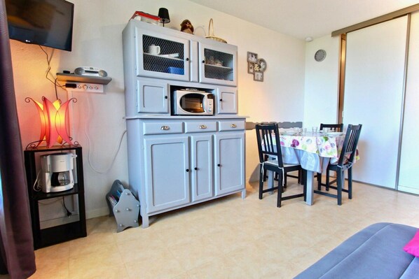 Un espacio habitable compacto con kitchenette, comedor y televisor montado en la pared.