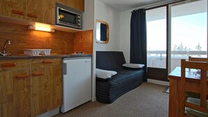 Habitación compacta con kitchenette, una cama con almohadas, ventana con cortinas y vistas al exterior.