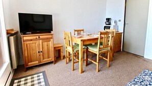 Un espacio habitable pequeño con una mesa de comedor de madera, cuatro sillas, un televisor sobre un mueble, una cafetera y un microondas.