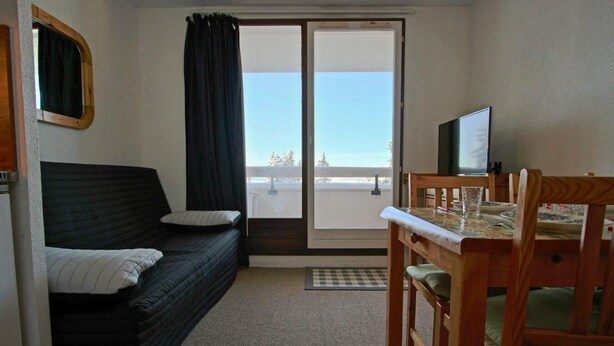 Una habitación pequeña con cama, una mesa de comedor con sillas, televisor y vista por una puerta corredera.
