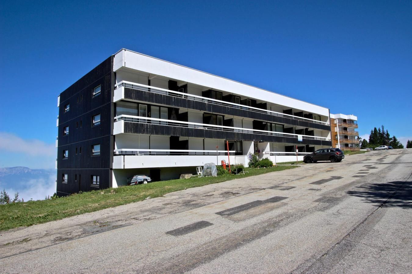 A multi-story hotel with balconies, a parking area, and a view of the mountains.