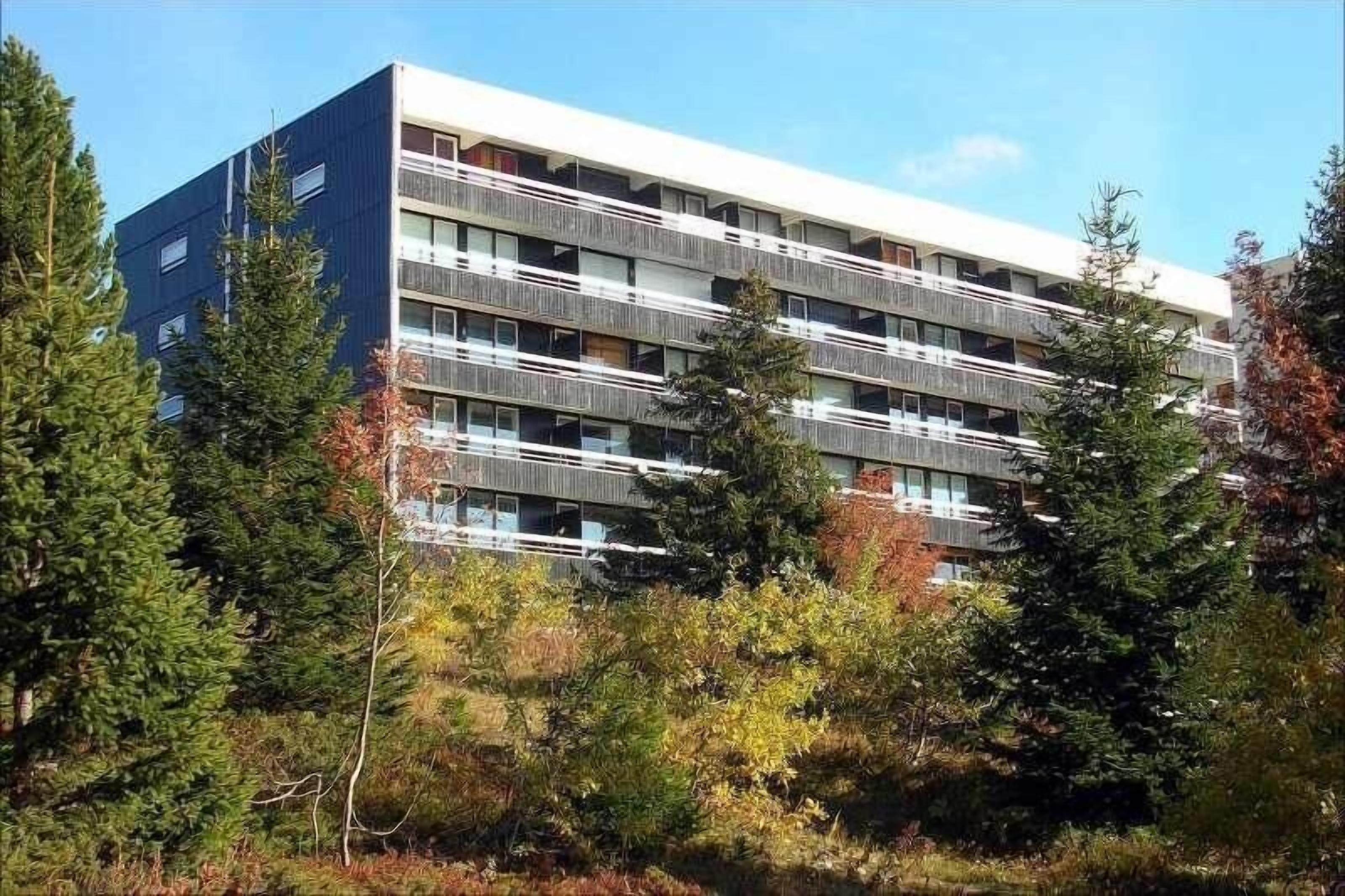 A multi-story building with balconies, surrounded by trees.