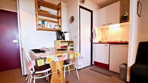 Kompakti oleskelutila, jossa on ruokapöytä, tuoleja, pieni keittiö ja pieni oleskelualue.