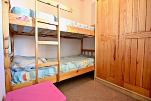 A bunk bed room with a wooden wardrobe and a pink storage box.
