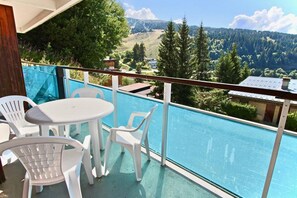 Een balkon met een zwembad, witte plastic stoelen en een tafel.