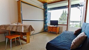 A room with a bed, a table with chairs, a TV on a wooden cabinet, and a large window with curtains. - 100m from ski slopes, Ground floor, 19m², Chamrousse (Chamrousse)