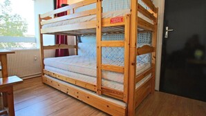 Un lit superposé avec une pancarte fixée sur la tête de lit, une fenêtre avec des rideaux, une table en bois et une porte.