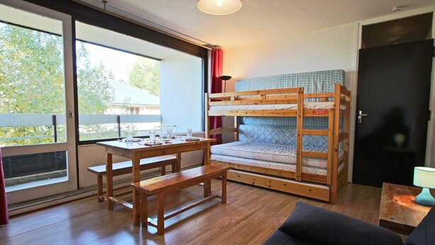 Une pièce avec un lit superposé, une table en bois avec des bancs, un canapé et une porte.